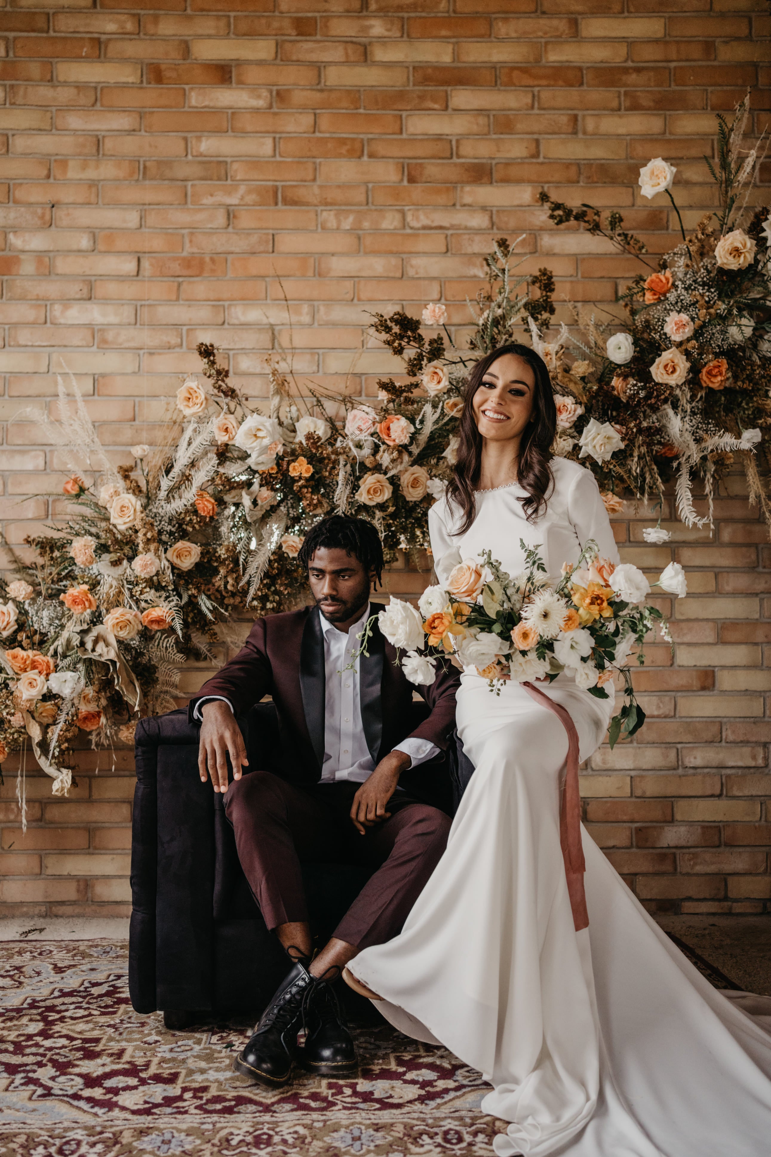 two people getting married, wedding, standing on and in front of a stone-wall holding a wedding-bouqet